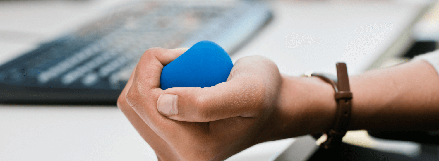 Close up of male worker squeezing a blue stress ball while working on a laptop computer.